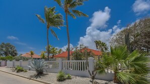 A residential area with palm trees, a white fence, and a building with a red roof.