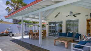 An outdoor patio with a wooden deck, a covered seating area with a sofa and chairs, and a ceiling fan.
