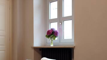 Un letto rifatto con lenzuola e asciugamani bianchi, una finestra con vista e un vaso con fiori sul davanzale.
