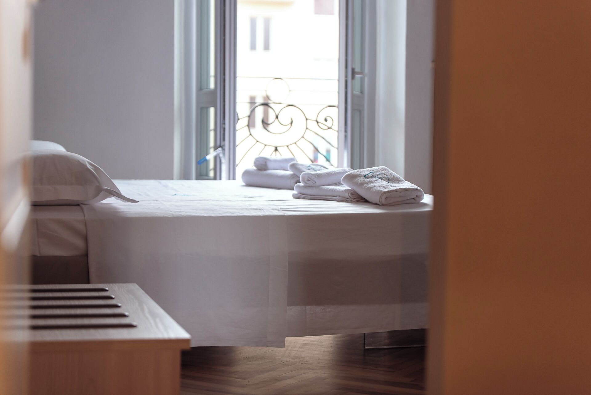 A neatly made bed with white linens and a set of folded towels on a wooden floor.