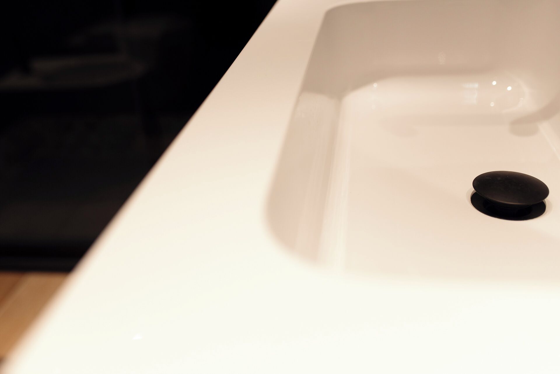 A close-up of a white sink with a black drain stopper.