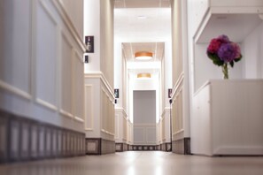A long, narrow hallway with a central light fixture and a flower arrangement at the end. - Gli Appartamentini del Bistrot dei Vinai (Cuneo)