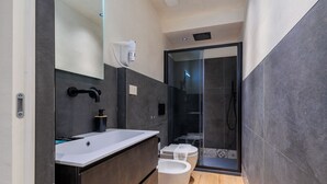 Um banheiro moderno com pia branca, armários escuros, box de vidro e vaso sanitário.