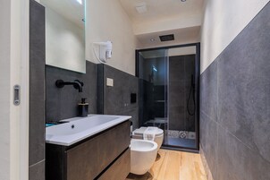Un baño moderno con un lavamanos blanco, muebles oscuros, cabina de ducha con vidrio y un inodoro.