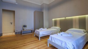 Quarto de hotel com duas camas, piso de madeira, porta branca e ar condicionado fixado na parede.