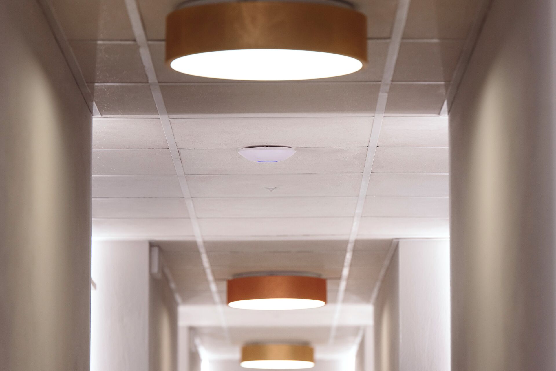 A corridor with ceiling-mounted lighting fixtures and a visible smoke detector.