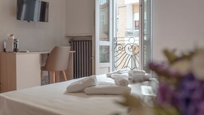 Quarto de hotel com cama, escrivaninha, cadeira, televisão e varanda com guarda-corpo.