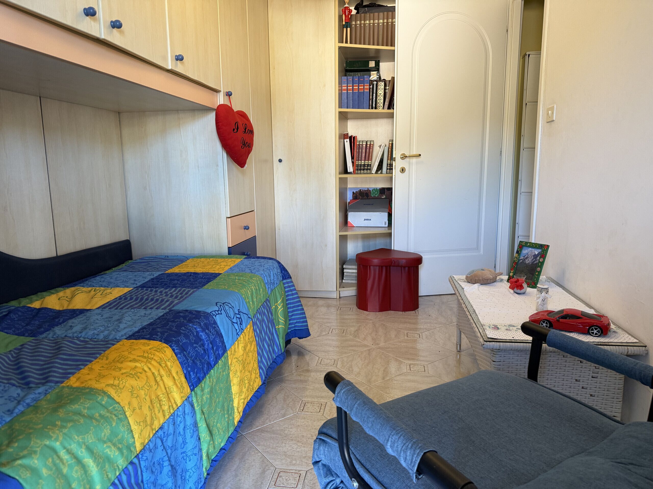 Ein Schlafzimmer mit zwei Betten, einem Bücherregal, einem kleinen Tisch mit einem Bilderrahmen und einer herzförmigen roten Dekoration.