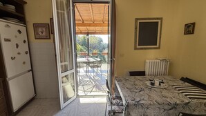 A room with a dining table, chairs, a radiator, a window, and a door leading to an outdoor area. - The Piano Apartment (Imperia)