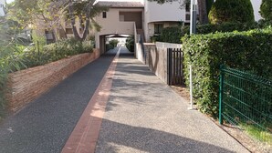 A pathway leading to a building with a tiled roof, surrounded by greenery and a brick wall. - Apartment with balcony near beach (Six-Fours-les-Plages)