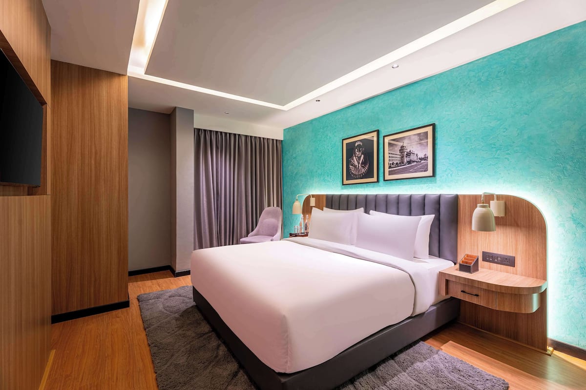 Une chambre d’hôtel moderne avec un grand lit, une table de chevet, un téléviseur fixé au mur et un mur d’accent de couleur turquoise.