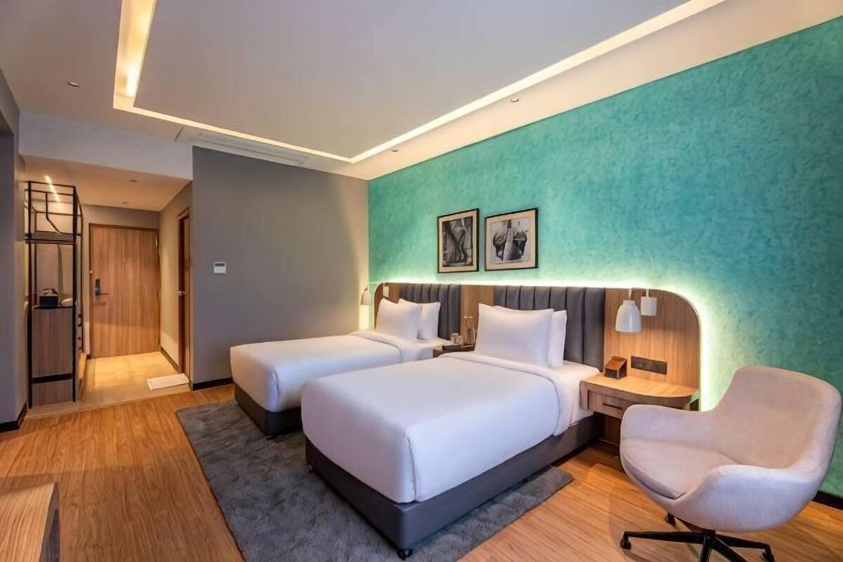 Une chambre d’hôtel avec deux lits, un bureau, une chaise et un mur vert à texture.