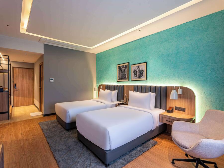 A hotel room with two beds, a desk, a chair, and a bathroom.
