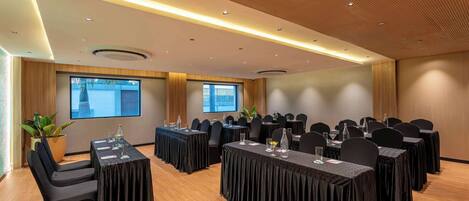 A conference room with multiple tables, chairs, and a large screen.