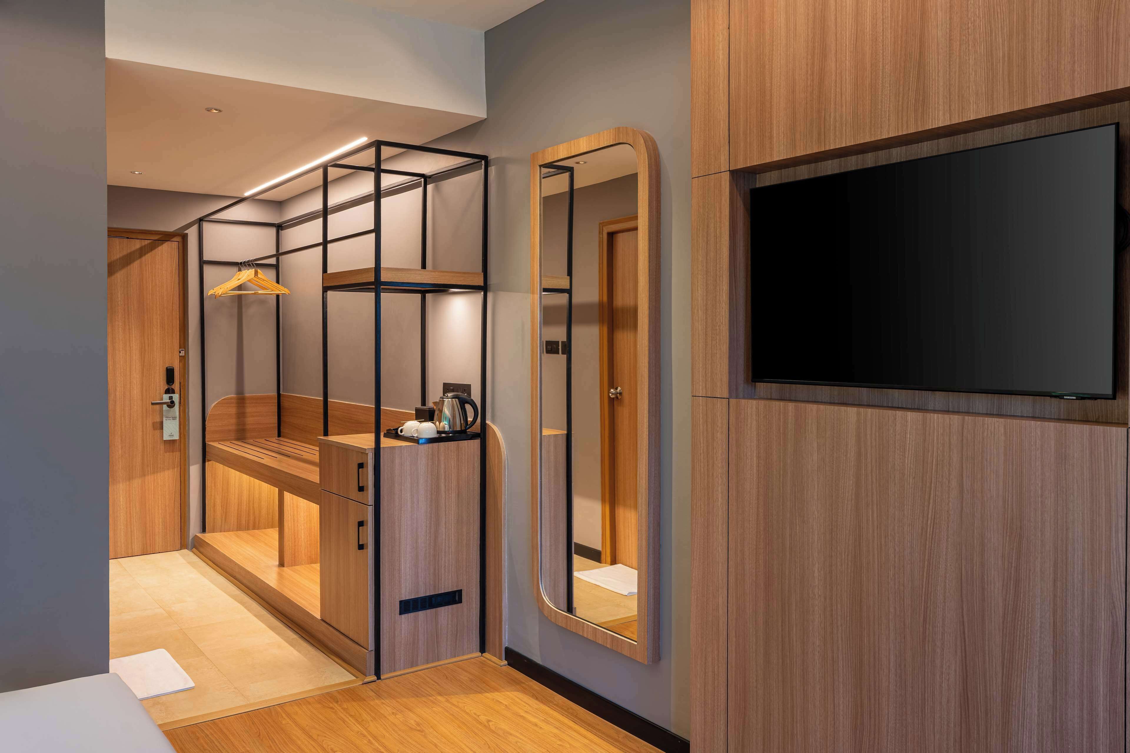Una habitación de hotel moderna con un armario de madera, un espejo y un televisor de pantalla plana.