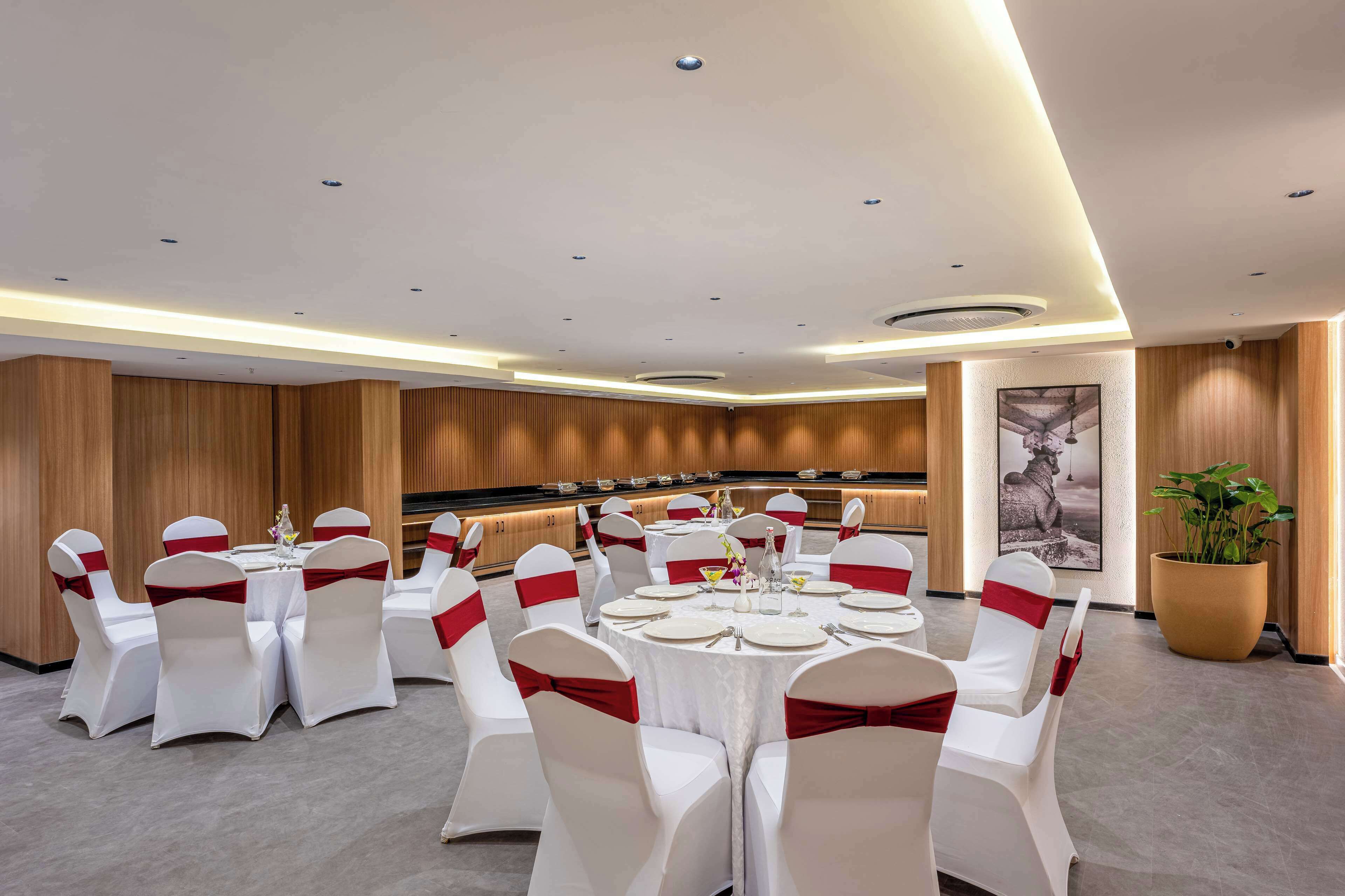 Une salle de banquet avec des tables rondes, des chaises blanches ornées de rubans rouges et un mur lambrissé en bois.