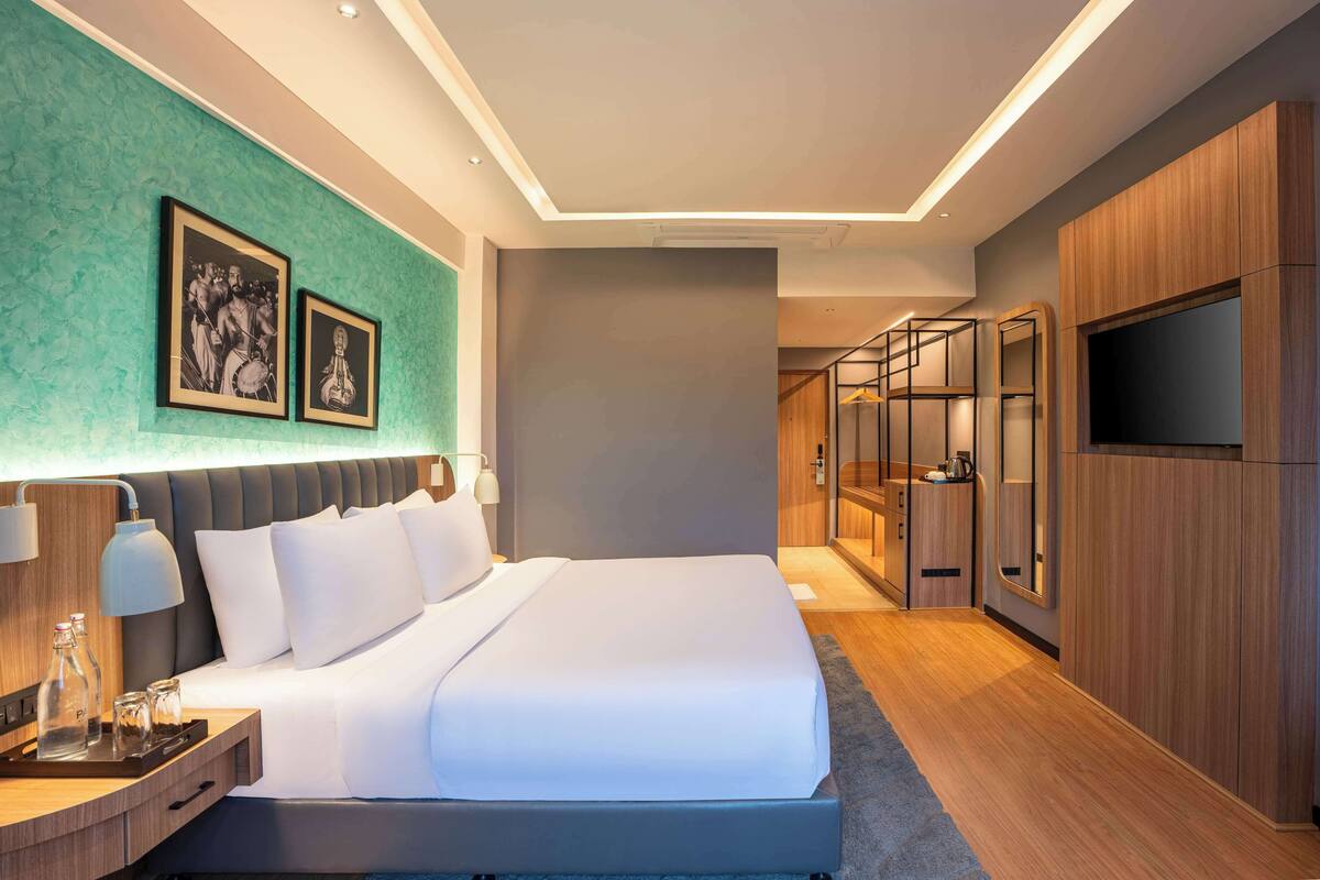 Une chambre d’hôtel moderne dotée d’un grand lit, de tables de chevet, d’un téléviseur à écran plat et d’un dressing.