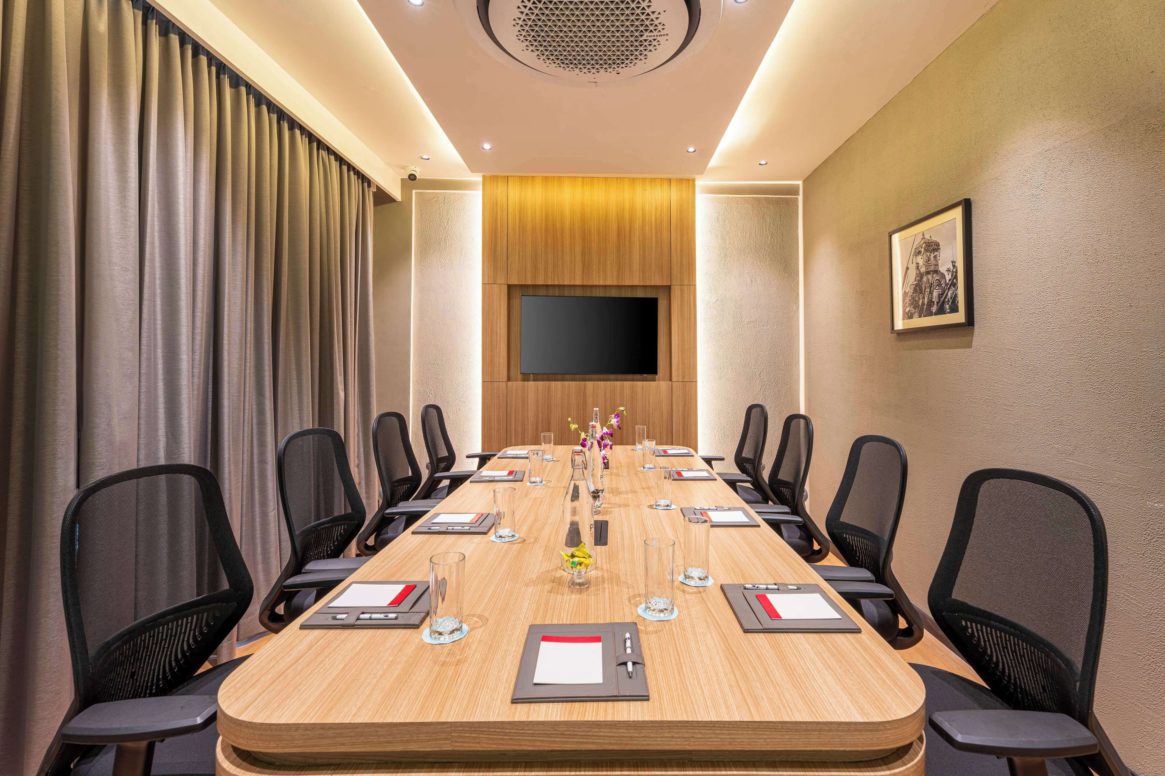 A conference room with a long table, black chairs, a flat-screen TV, and a framed picture on the wall.
