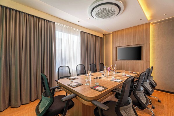 A conference room with a long table, chairs, a flat-screen TV, and a ceiling-mounted smoke detector.