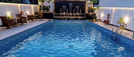Una piscina con fuente escalonada, rodeada de sillas de descanso y plantas en macetas.