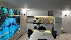 A modern kitchen with a large wall-mounted TV displaying a waterfall scene, a dining area with a marble table and black chairs, and a compact refrigerator. - Duplex two bedroom apartment (Tbilisi)