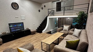 A modern living room with a curved ceiling, a staircase, and a flat-screen TV. - Duplex two bedroom apartment (Tbilisi)