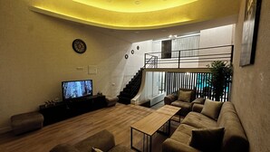 A modern living room with a flat-screen TV, a sofa set, a coffee table, and a staircase leading to an upper level. - Duplex two bedroom apartment (Tbilisi)