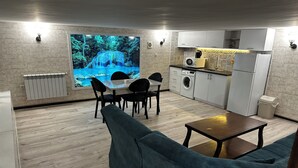 A modern kitchen with a built-in washing machine, a dining area with a table and chairs, and a large wall-mounted TV displaying a waterfall scene. - Duplex two bedroom apartment (Tbilisi)