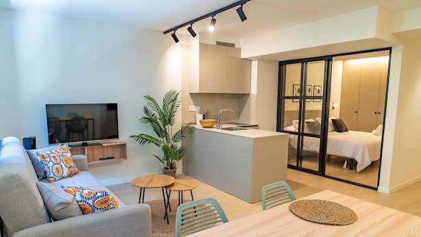 Una sala de estar moderna con sofá, televisor, mesa de comedor y zona de cocina.