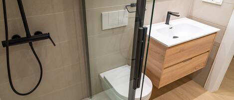 Un baño moderno con cabina de ducha de vidrio, un inodoro blanco, un mueble de tocador de madera con lavamanos y un espejo sobre el mueble.