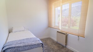 Een kleine, schone kamer met een bed, een radiator en een raam met jaloezieën.