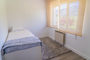 A small, clean room with a bed, a radiator, and a window with blinds.