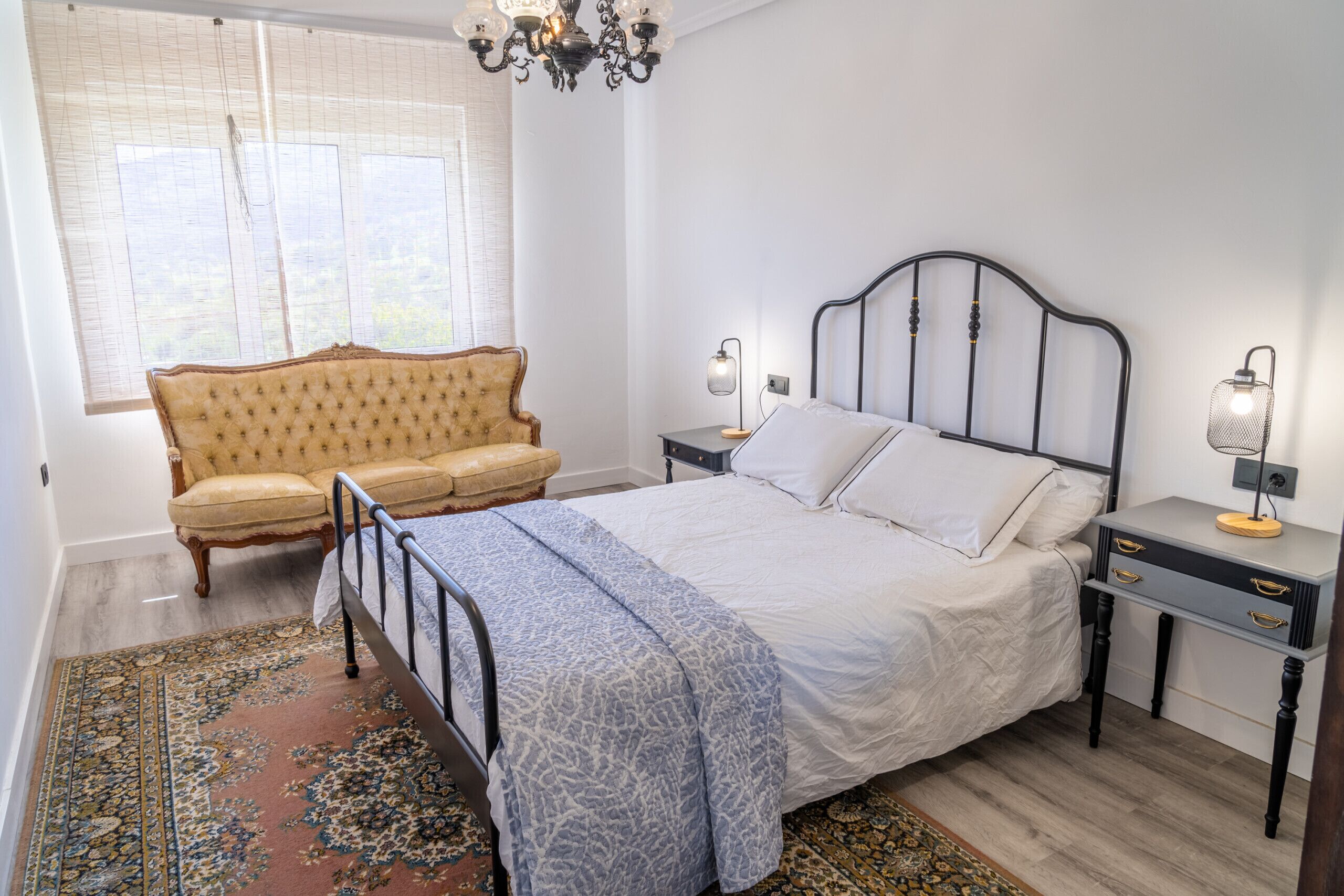 Un dormitorio con cama, mesitas de noche, lámpara, silla y ventana con persianas.