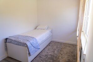 A small, single-bed room with a grey carpet, white walls, and a window with a white blind. - Beautiful Rural House in Nava (Nava)