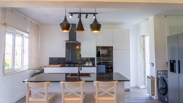 Een moderne keuken met een centraal eiland, drie hanglampen en een inbouwoven.