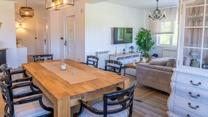 Een eethoek met een houten tafel en stoelen, een aan de muur bevestigde televisie en een kroonluchter.