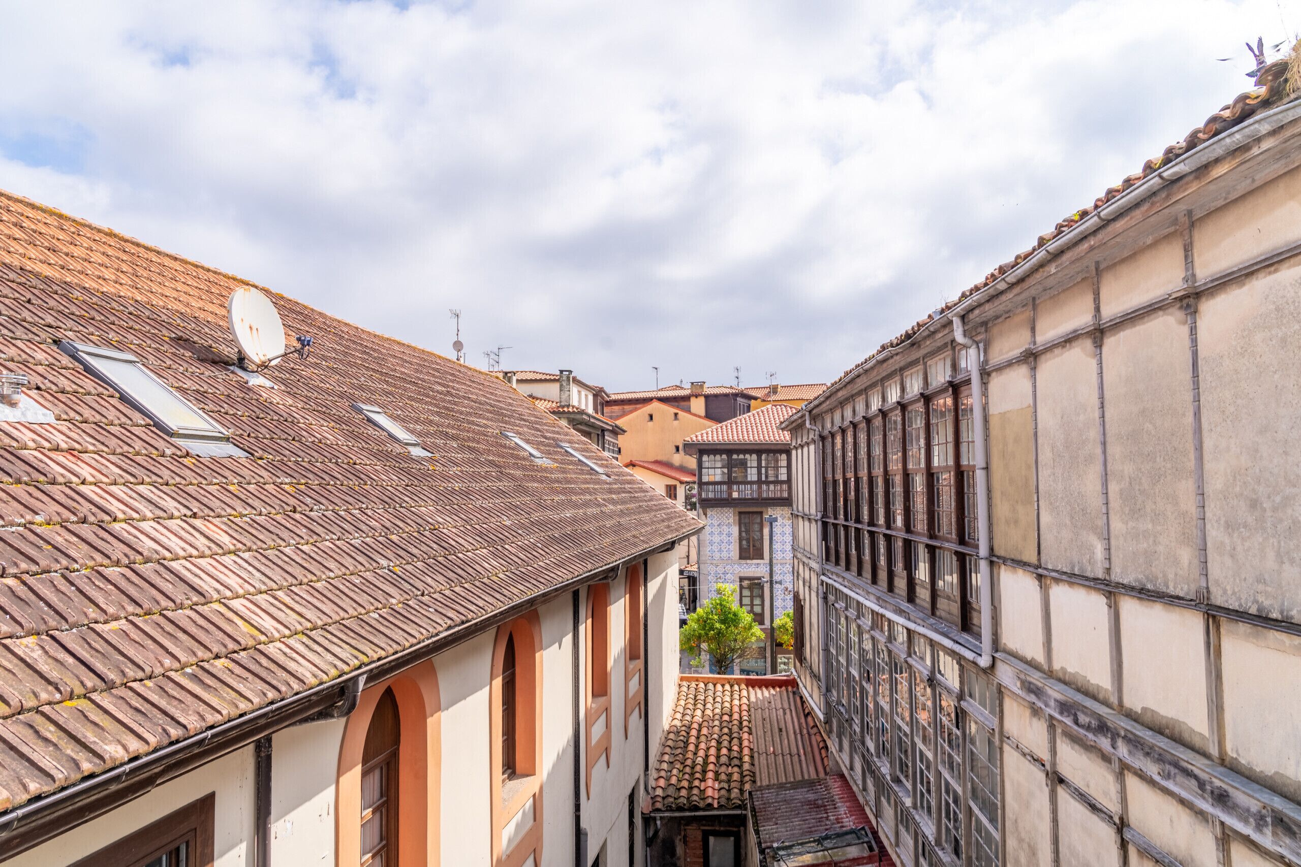 A narrow street with traditional buildings, a visible satellite dish, and a tiled roof.