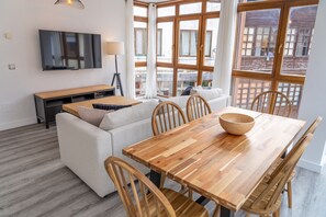 A modern living room with a wooden dining table, white sofa, and a TV mounted on the wall. - Spacious Apartment in the Heart of Llanes (Llanes)