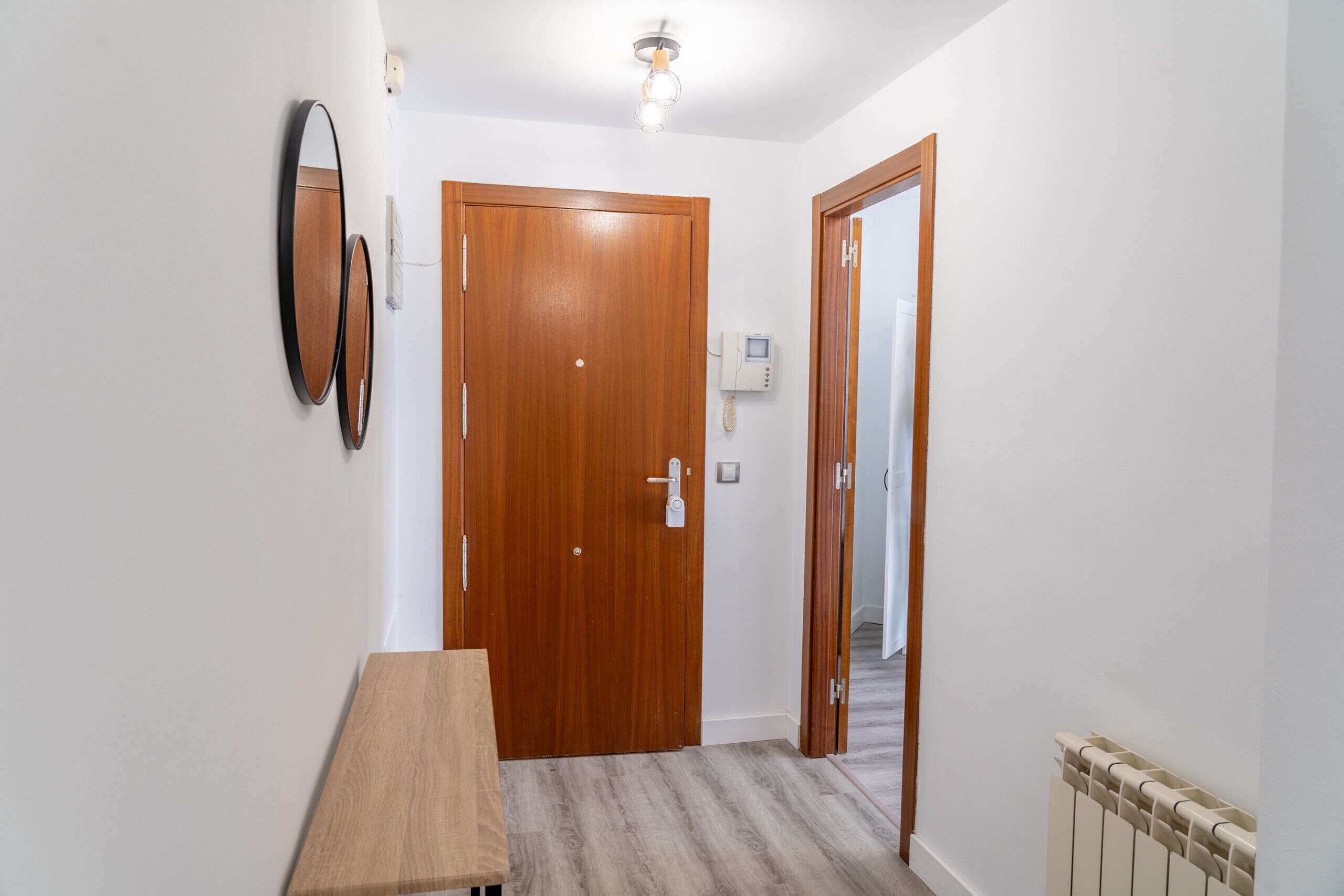 Un couloir avec une porte en bois, une petite table, un miroir fixé au mur et un radiateur.