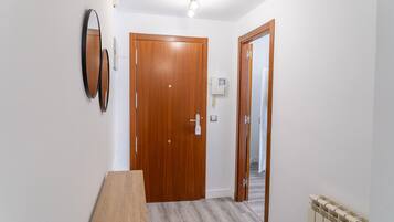 Un couloir avec une porte en bois, une petite table, un miroir fixé au mur et un radiateur.