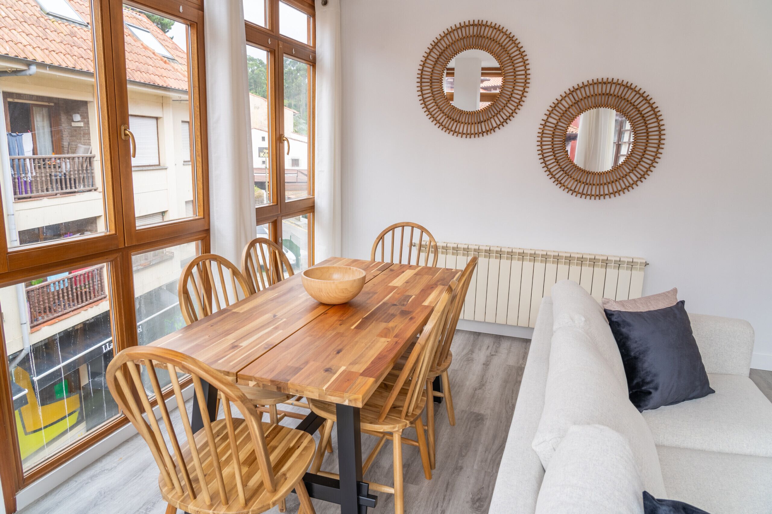 A dining area with a wooden table and chairs, a white sofa, and two wall mirrors.