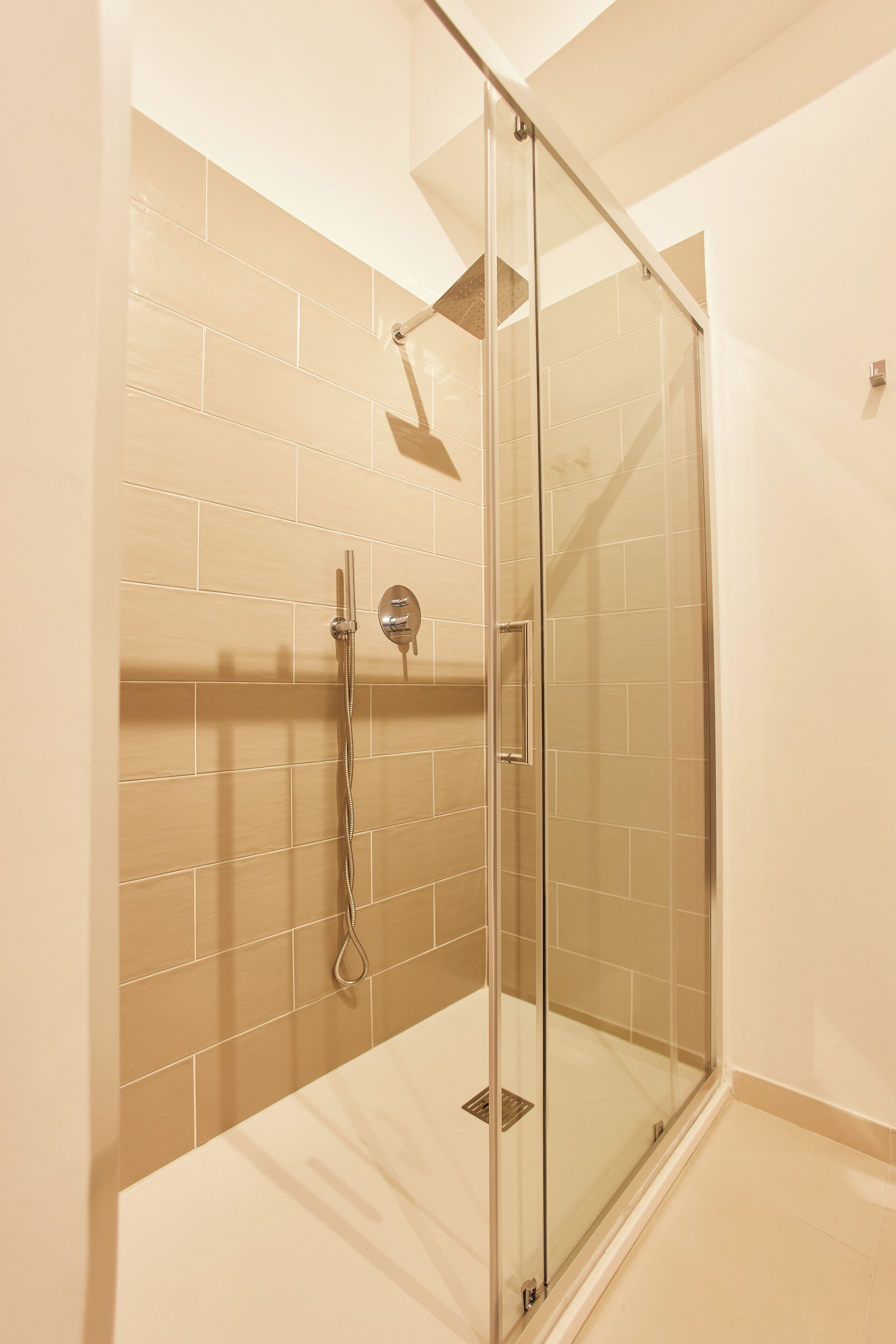 A glass-enclosed shower with a handheld showerhead and a wall-mounted control panel.