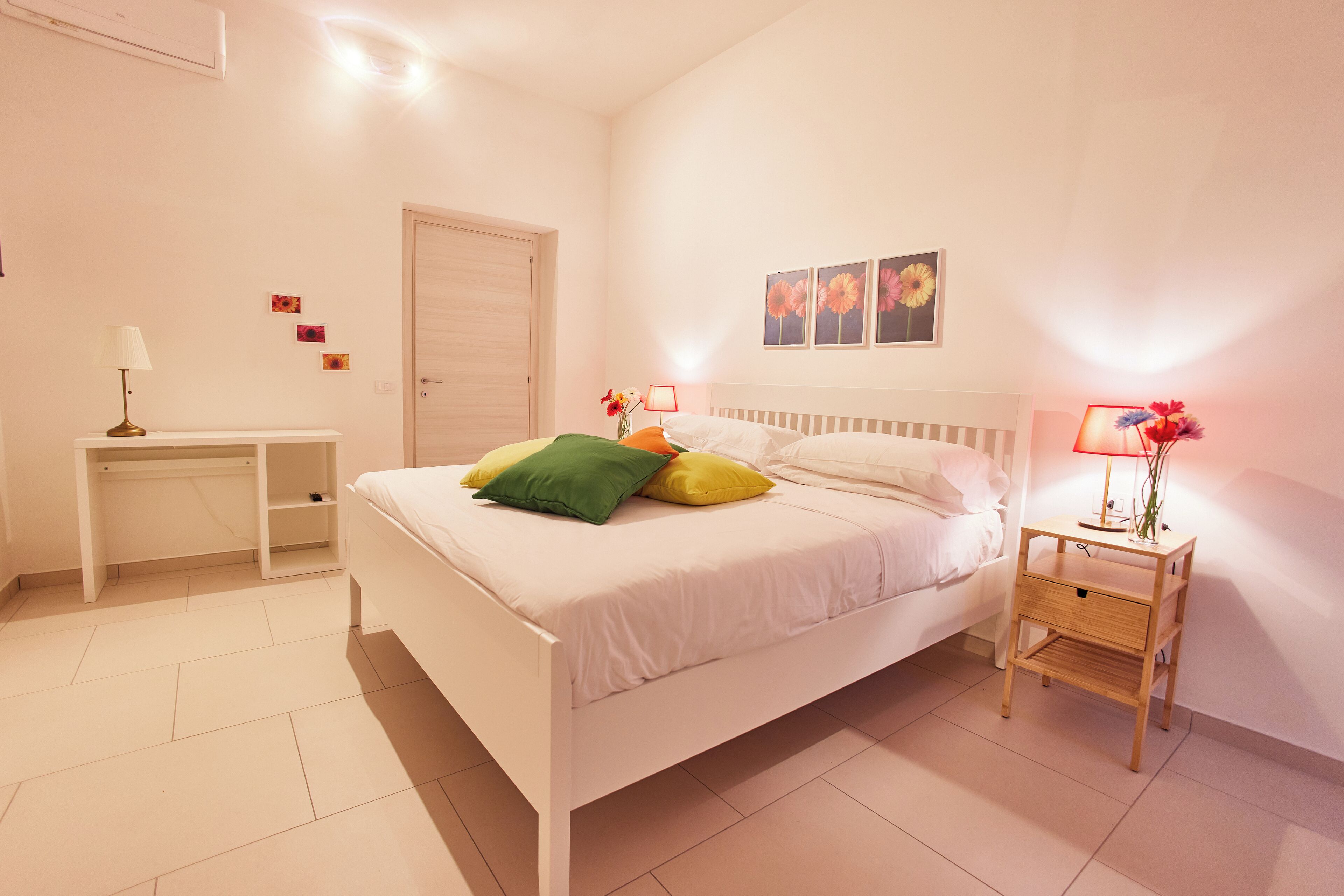 A bedroom with a bed, bedside tables, a desk, and a door.