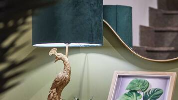 Une lampe ornée d’un motif de paon, une plante en pot encadrée et un miroir posé sur une étagère.