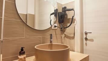A bathroom with a round mirror, beige tiles, a sink, and a hairdryer on the wall.