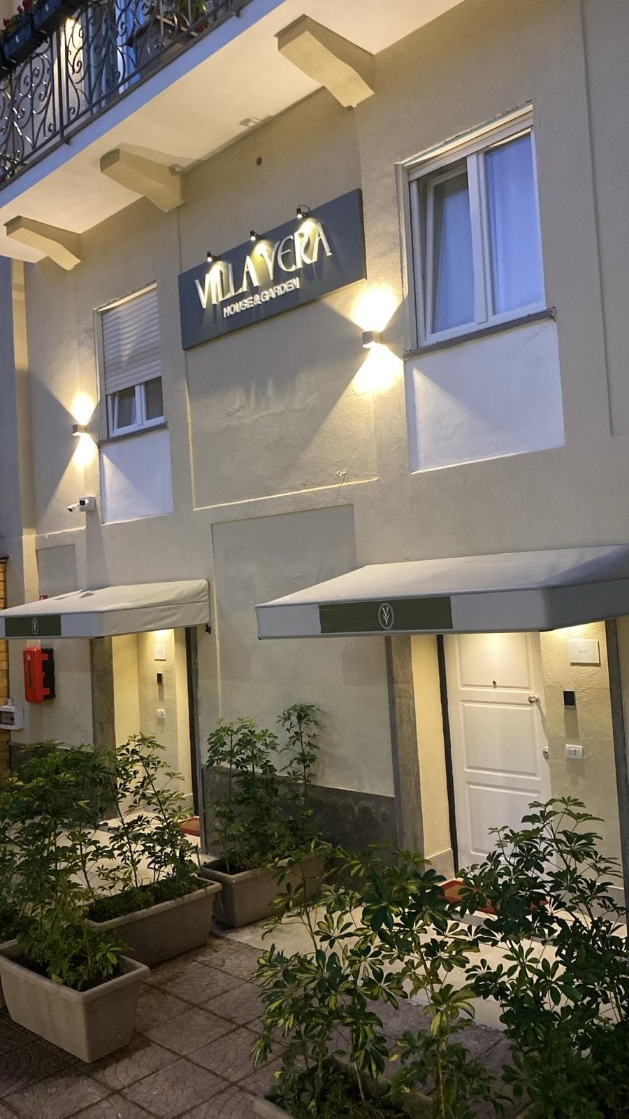 Un bâtiment sur lequel on peut lire l’inscription « Villa Vera », et qui dispose d’un espace extérieur abrité avec des plantes en pot.