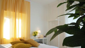 A neatly made bed with yellow and white pillows, a bedside table with a lamp, and a large green plant in a modern hotel room. - Villa Vera (Salerno)