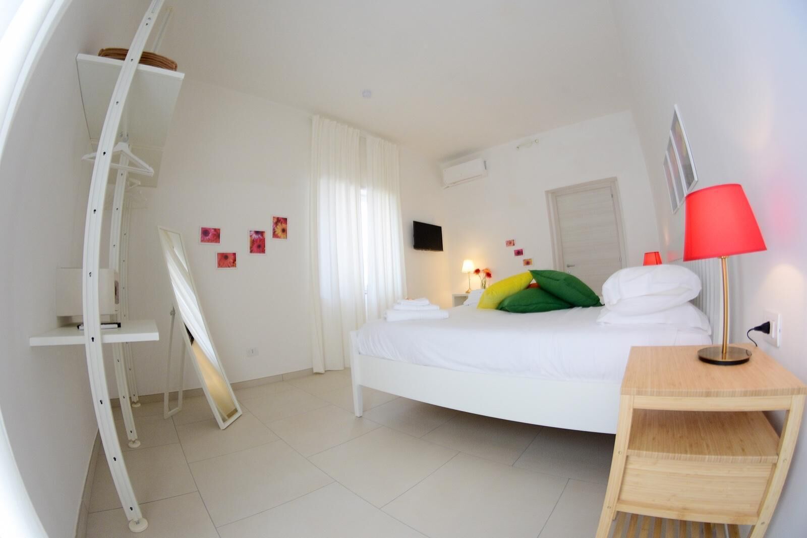 Une chambre d’hôtel moderne avec un lit aux courbes élégantes, une literie blanche, une lampe rouge et une petite table d’appoint en bois.