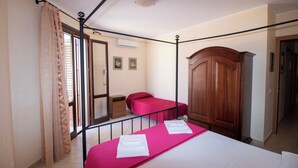 Un dormitorio con dos camas, un armario de madera, una mesita pequeña y una ventana con cortinas.