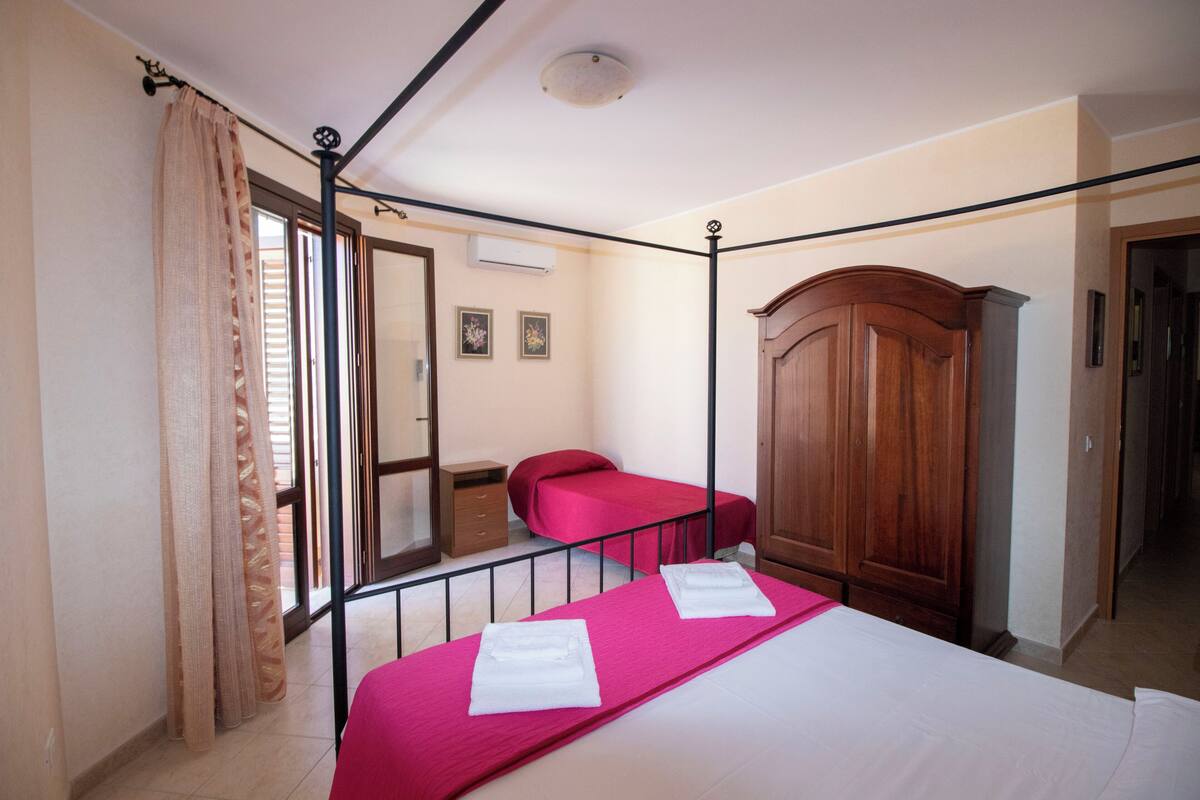 A bedroom with two beds, a wooden wardrobe, a small table, and a window with curtains.